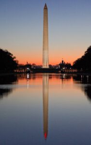 Washington Obelisk during sunrise, reflected in water.